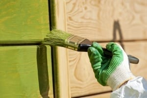hand with a paint brush painting wooden wall in green